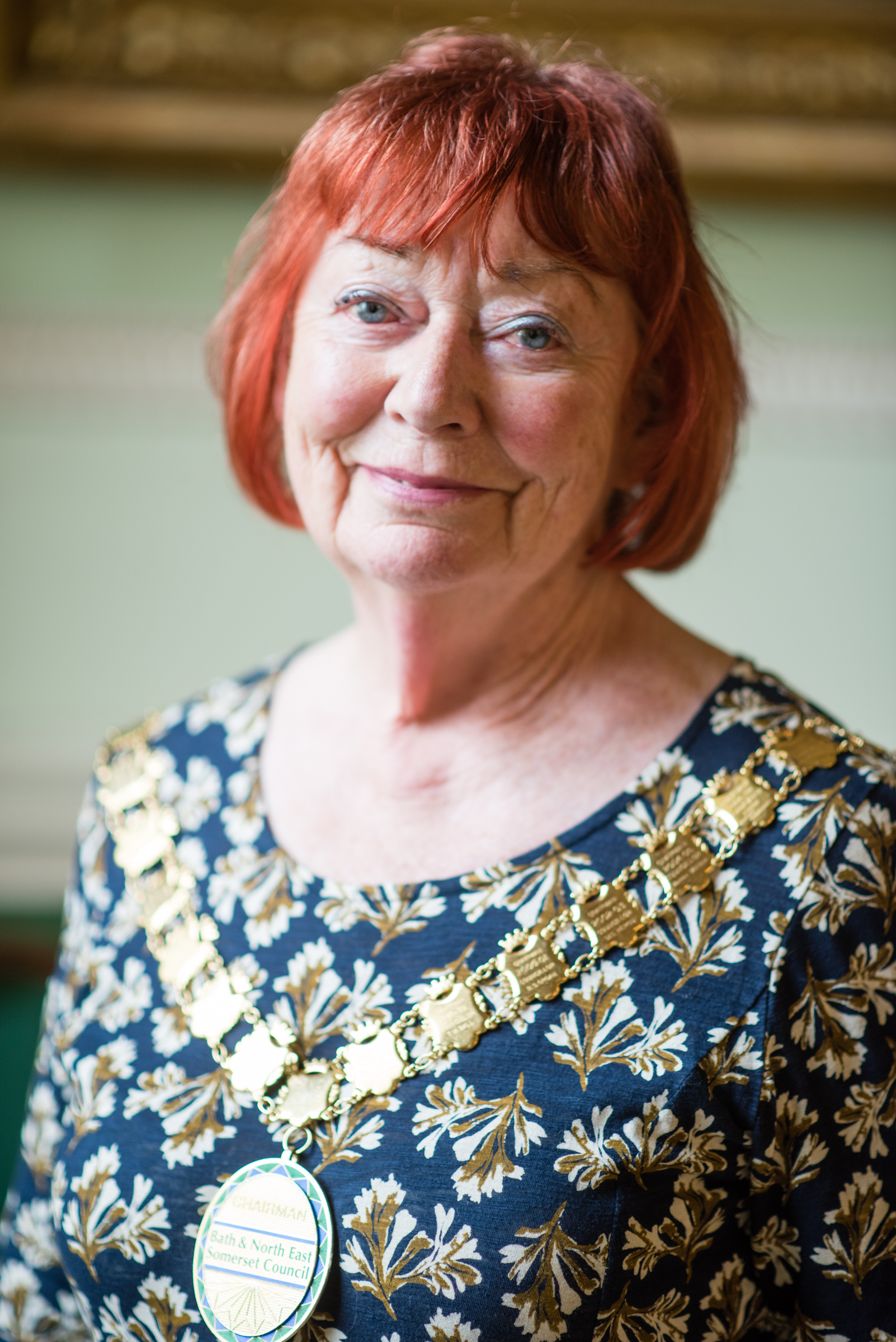 A portrait image of Councillor Liz Hardman, a redhaired lady in a floral print dress with the chain of office over her shoulders